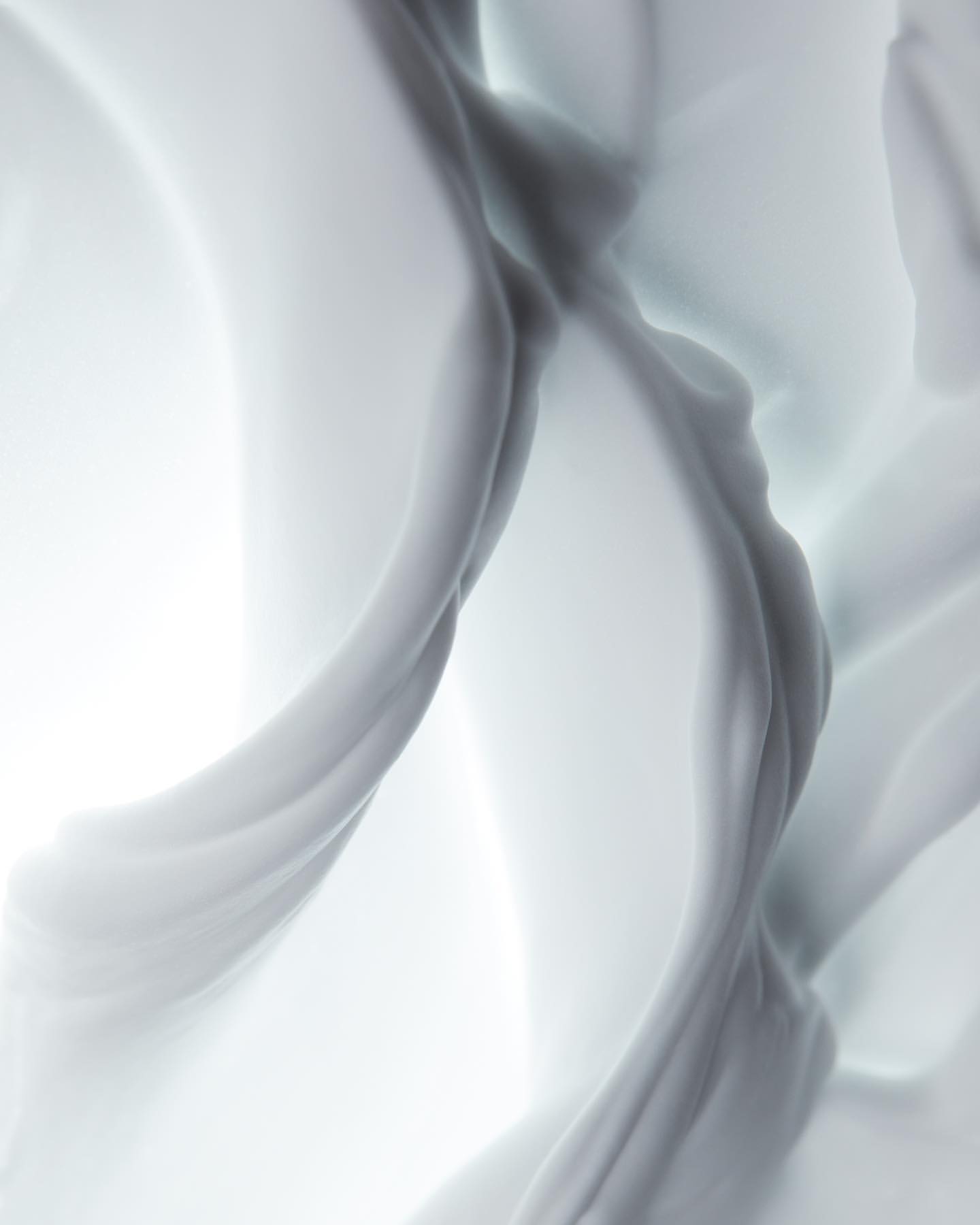 Abstract, swirling fabric in shades of white and grey creates a visually soft and flowing composition with a bright background.