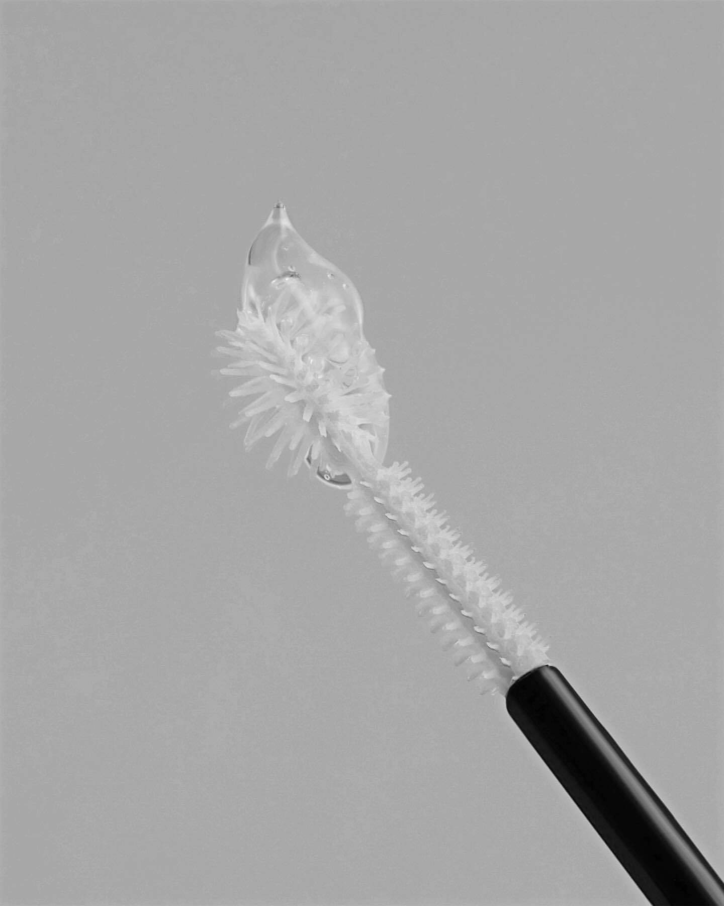 Close-up studio shot of a mascara wand brush with clear gel on the tip, showcasing beauty product application and cosmetic texture.