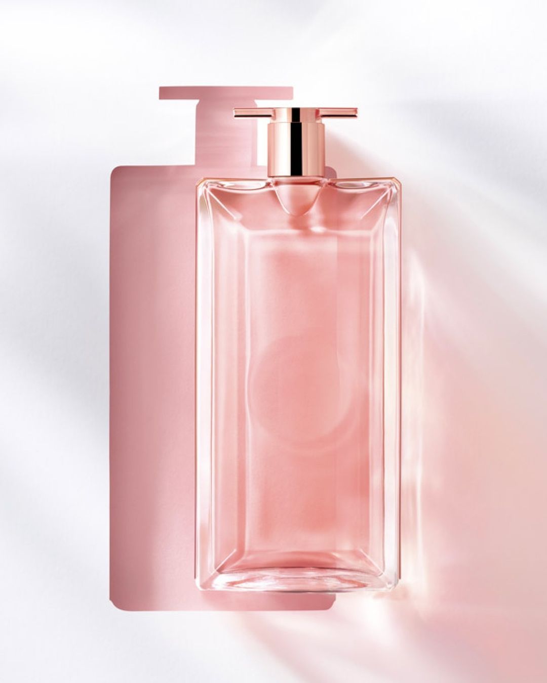 Close-up studio shot of a clear glass perfume bottle with a pink liquid inside, casting a shadow on a white background.