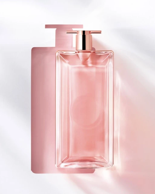 Close-up studio shot of a clear glass perfume bottle with a pink liquid inside, casting a shadow on a white background.