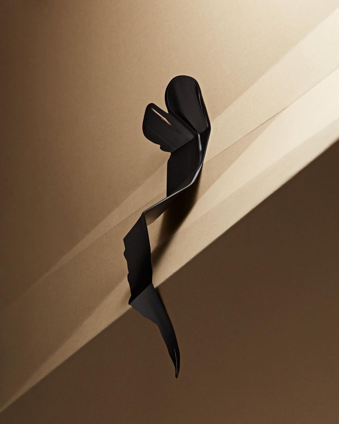 Abstract photograph of a curled black ribbon against a gradient brown backdrop, creating geometric shadows and a sense of depth.