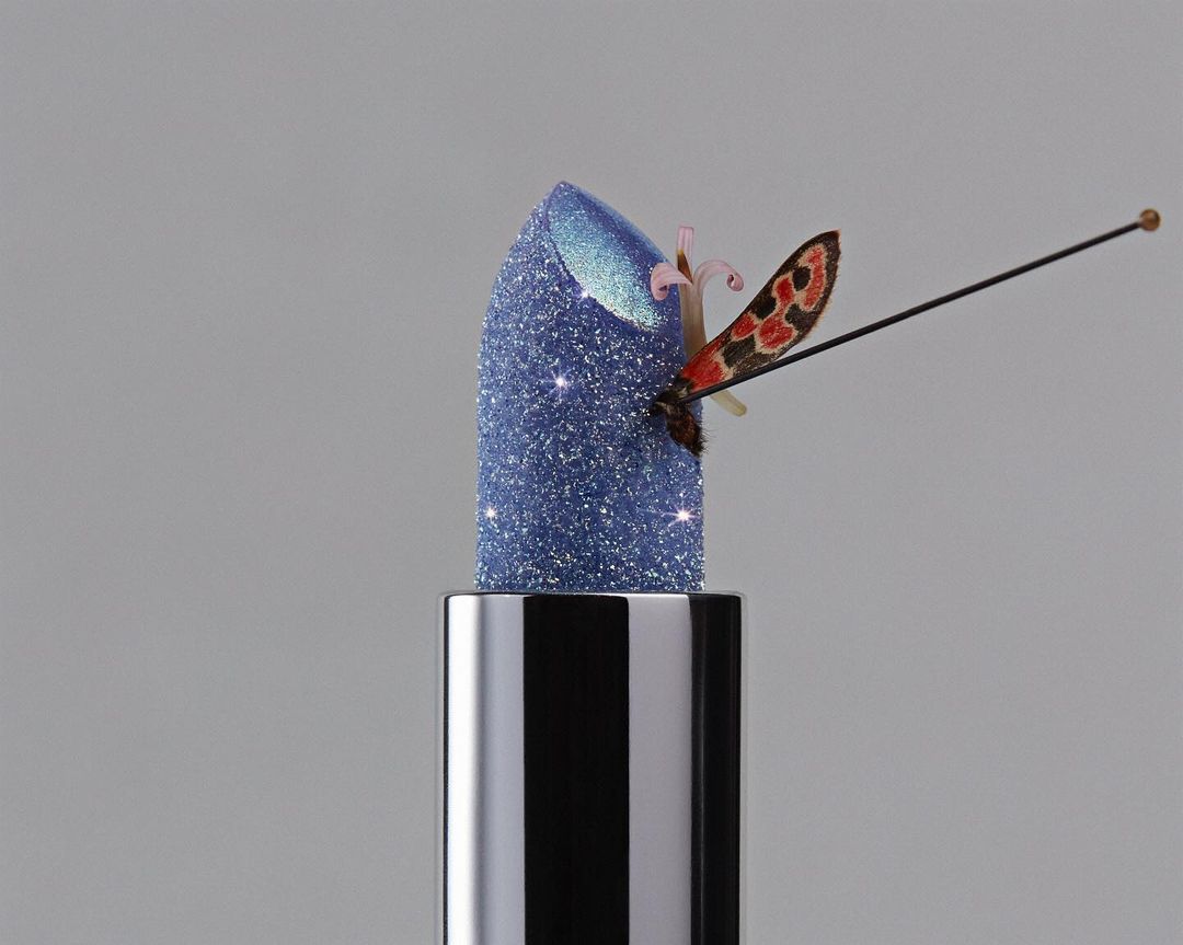 Close-up of blue glitter lipstick with a decorative butterfly against gray background in beauty, fashion and cosmetics style.