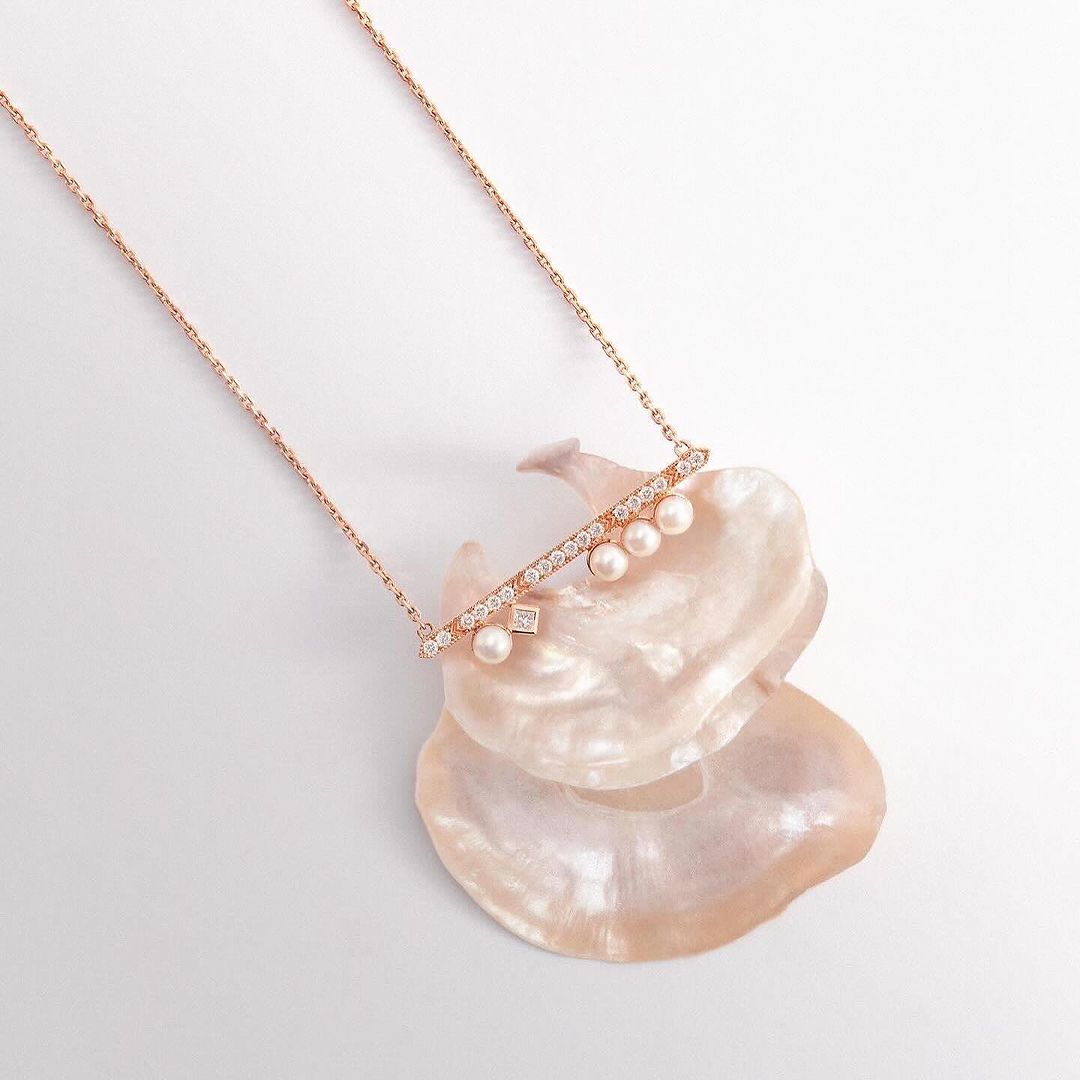Elegant rose gold necklace with pearls and diamonds resting on a textured seashell, creating a luxurious and delicate jewelry still life.