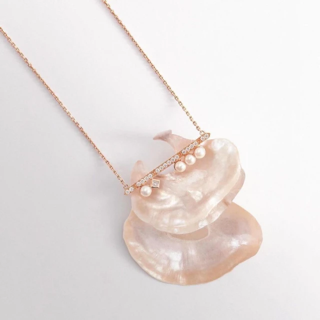 Elegant rose gold necklace with pearls and diamonds resting on a textured seashell, creating a luxurious and delicate jewelry still life.
