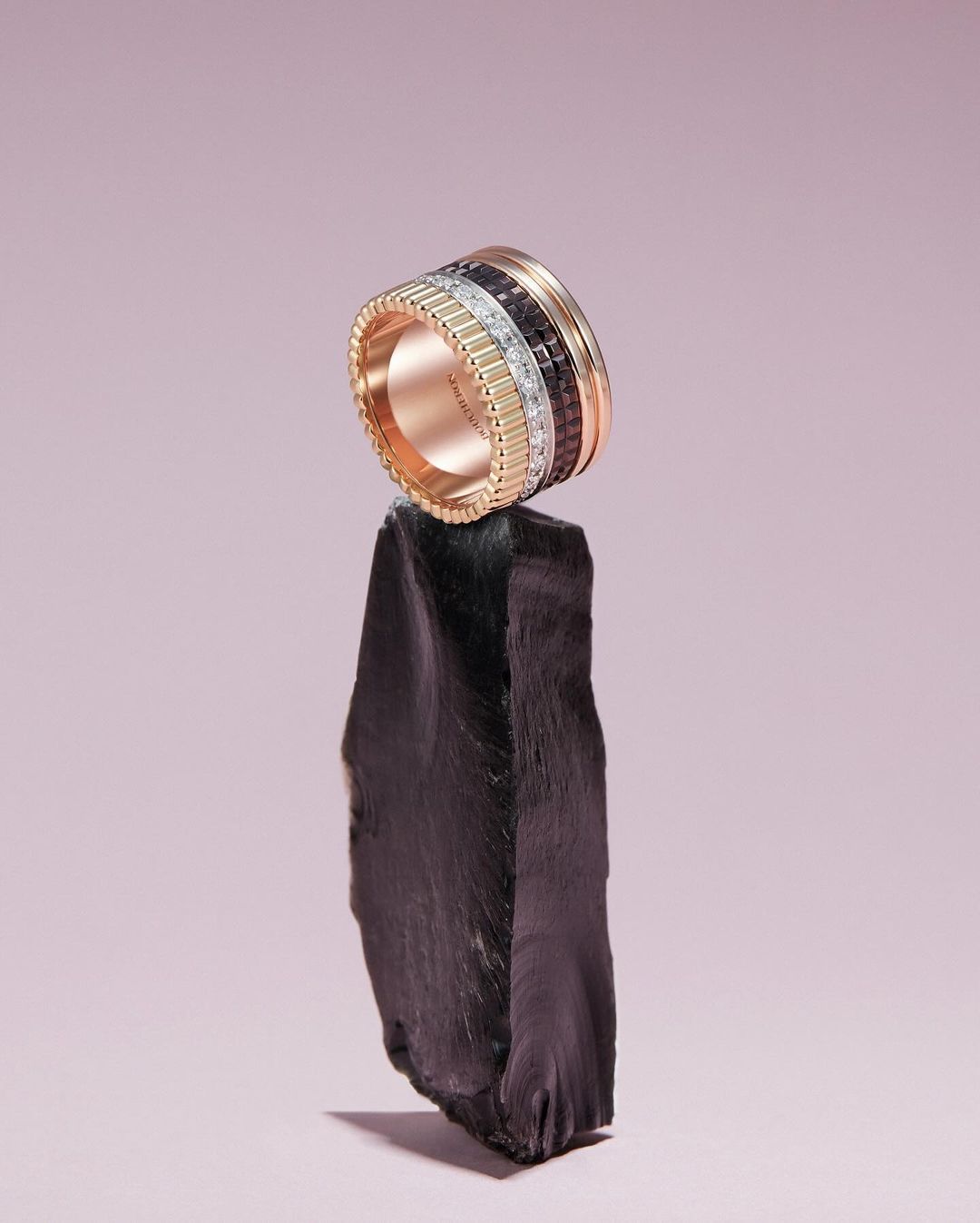 High-fashion jewelry shot: A luxurious diamond ring in rose gold is displayed on a rough rock, set against a light purple background.