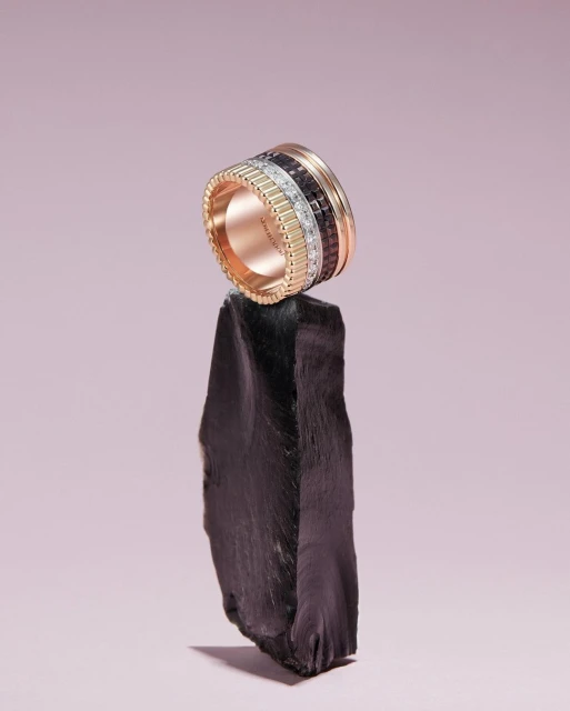 High-fashion jewelry shot: A luxurious diamond ring in rose gold is displayed on a rough rock, set against a light purple background.