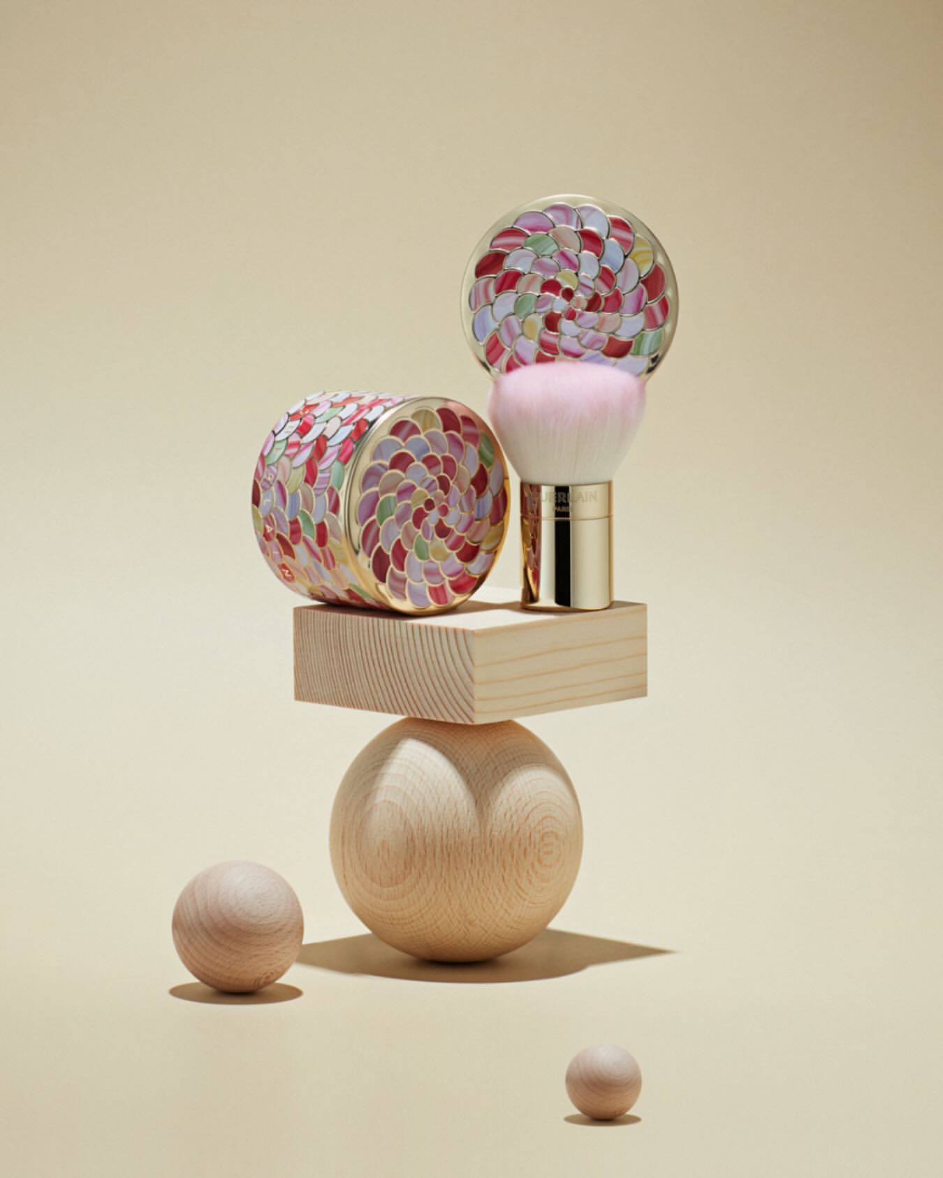 Cosmetic brush kit on a wooden geometric sculpture against a tan background, minimal studio beauty shot for a luxury beauty product.