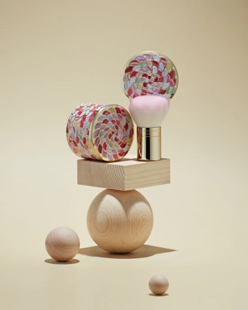 Cosmetic brush kit on a wooden geometric sculpture against a tan background, minimal studio beauty shot for a luxury beauty product.