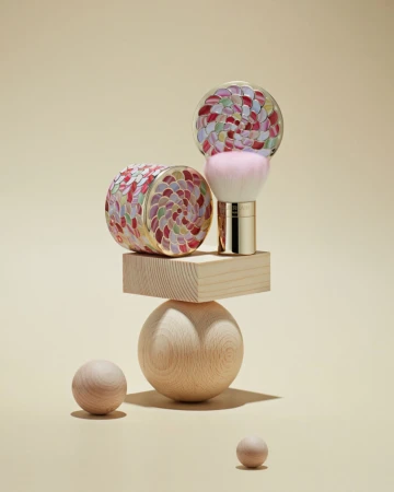 Cosmetic brush kit on a wooden geometric sculpture against a tan background, minimal studio beauty shot for a luxury beauty product.