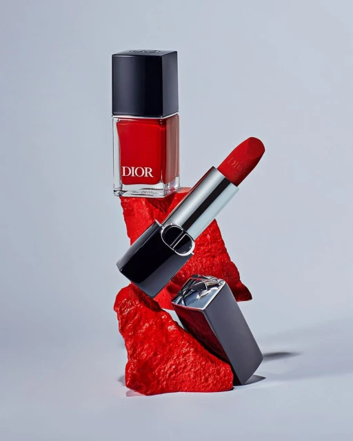 Still life shot of Dior nail polish and lipstick, stacked on red textured platforms, product photography in a light grey setting.