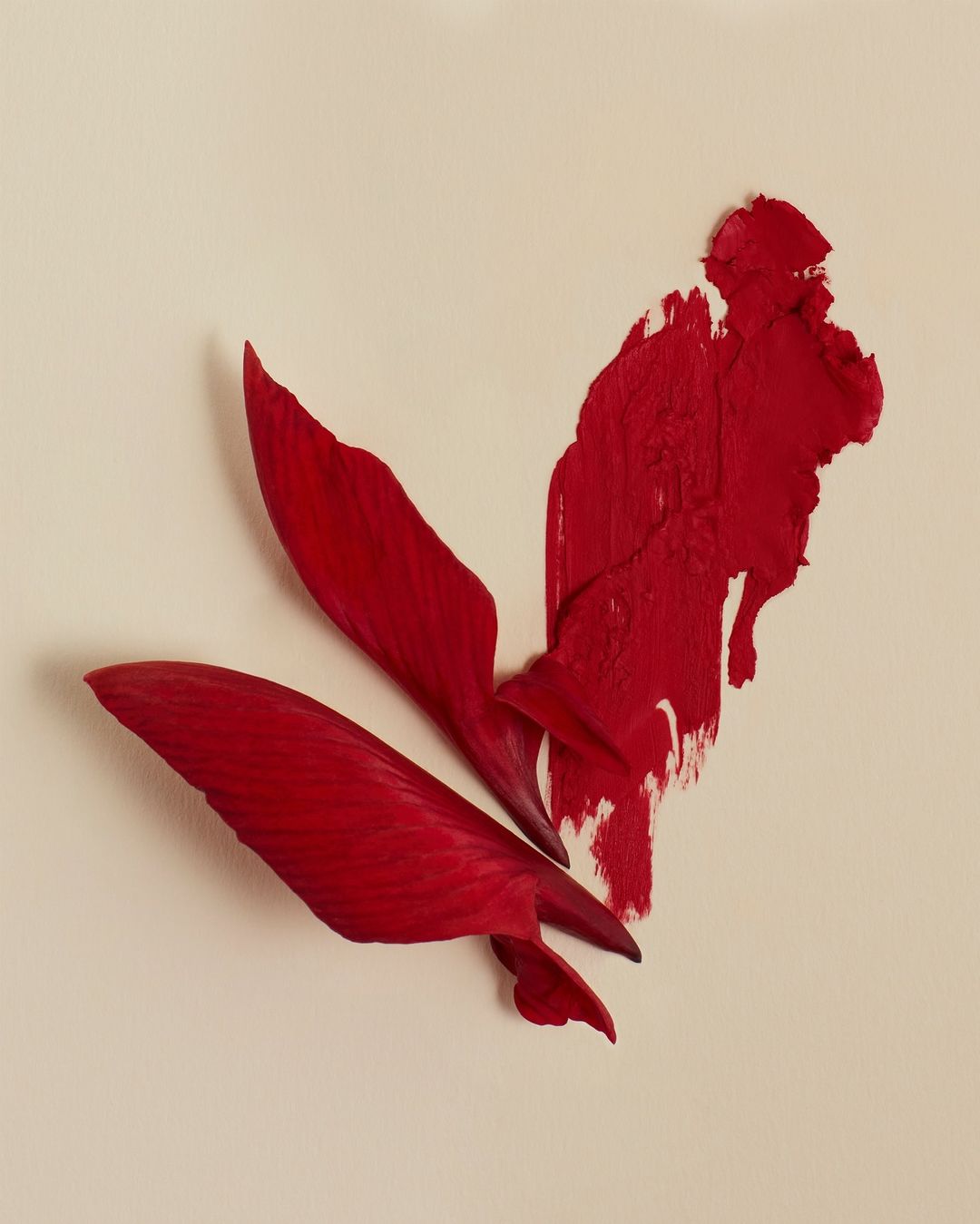 Abstract close-up of vibrant red lipstick smear and petals on a neutral beige background, conveying modern cosmetic artistry.