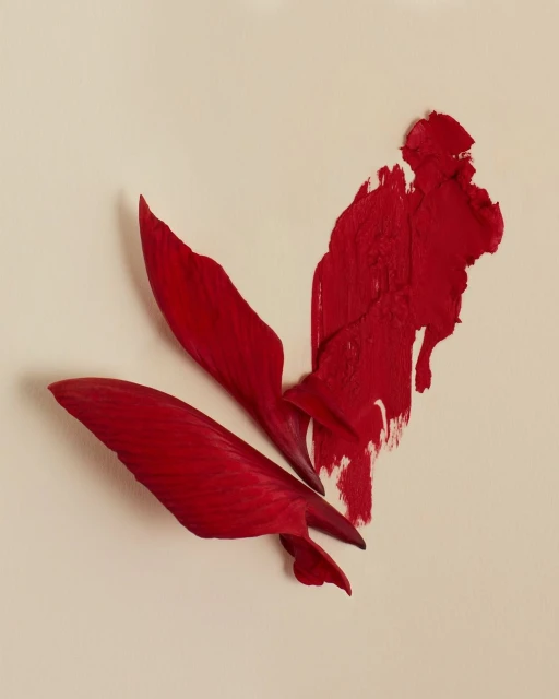 Abstract close-up of vibrant red lipstick smear and petals on a neutral beige background, conveying modern cosmetic artistry.