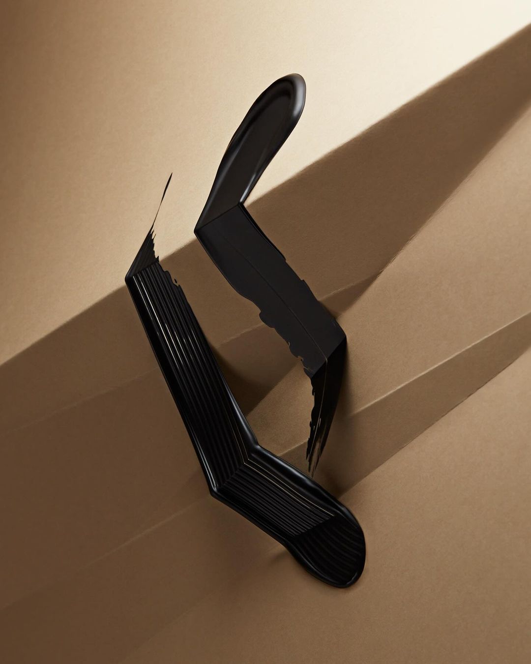 Bold artistic studio shot of a sleek black mascara wand and creamy smudge on a light tan angled staircase background with shadows.
