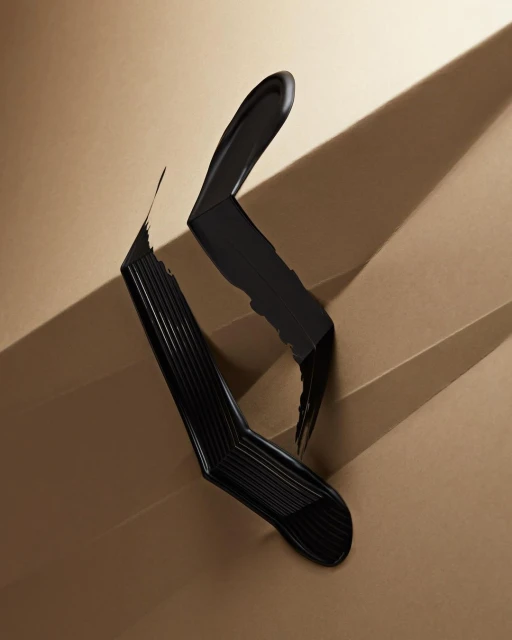 Bold artistic studio shot of a sleek black mascara wand and creamy smudge on a light tan angled staircase background with shadows.