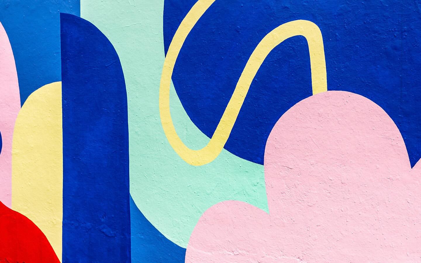 Abstract painting on textured wall featuring bold geometric shapes in pink, blue, yellow, red, and green, creating a vibrant, colorful design.