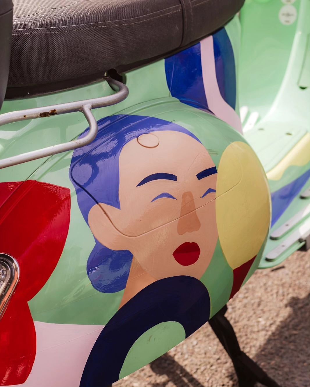 Close-up of a scooter with colorful graphics, including a person's face, in shades of green, blue, red, and tan; the seat is black.