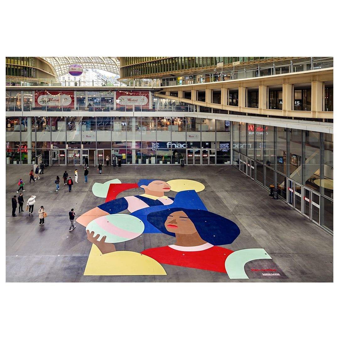 Illustration on plaza of two women with hats in front of a commercial building in Paris, France. People walk through plaza.