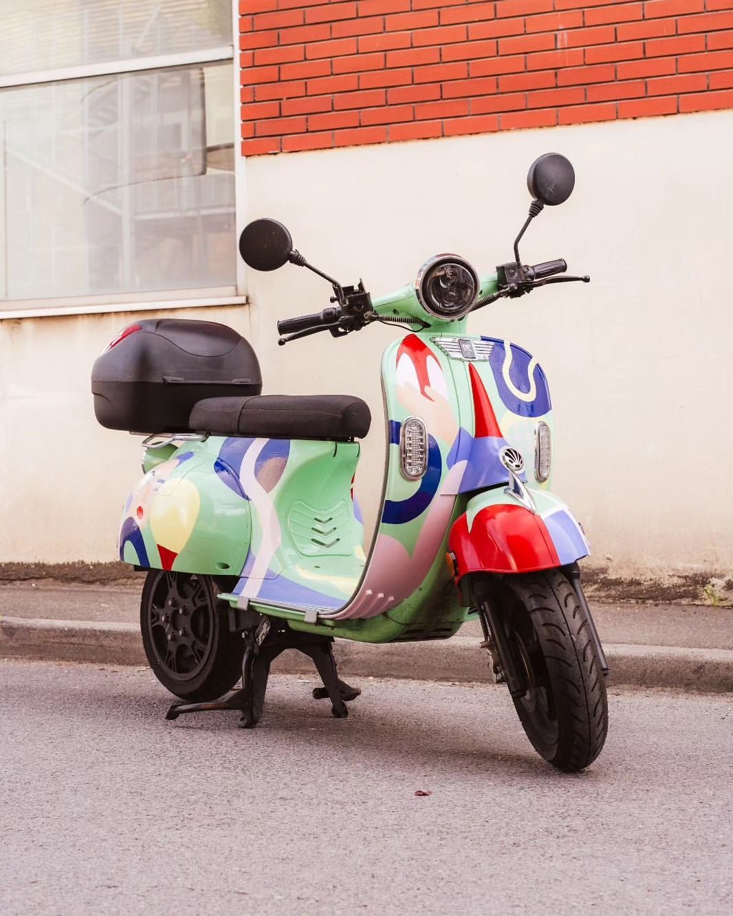 Colorful patterned scooter parked outdoors near a brick wall, showcasing its unique design and modern features.