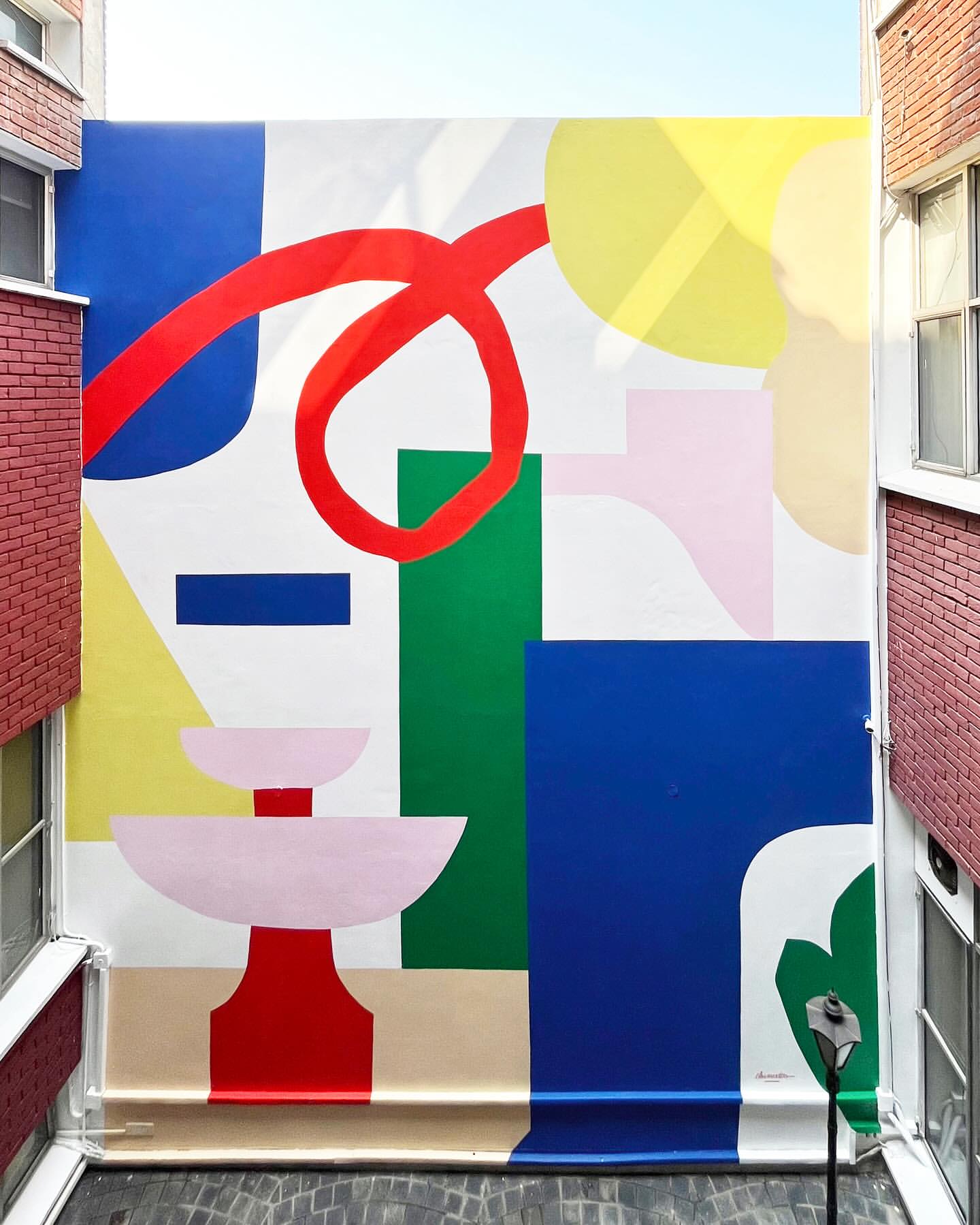 Eye-level outdoor shot of abstract wall art featuring geometric shapes and bold colors, including red, green, blue, yellow, and pink.