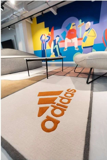 Interior design featuring an Adidas logo rug, modern furniture, and colorful mural in a retail or showroom environment.