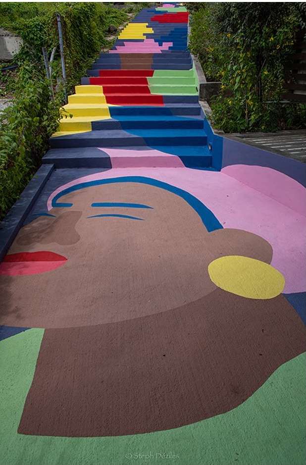 A staircase transformed into an art installation, featuring a large-scale painted portrait and vibrant, colorful steps in an urban setting.