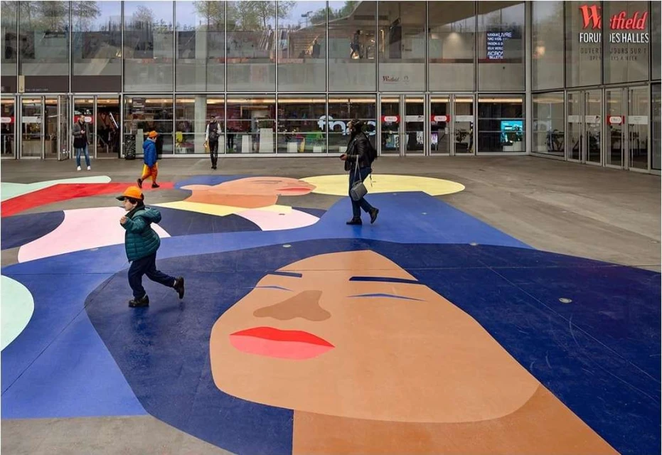 Child runs in front of Westfield Forum des Halles shopping center on colorful ground mural in Paris, France on an overcast day.