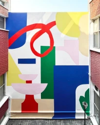 Large colorful abstract mural painted on an exterior building wall with geometric shapes in blue red green and yellow