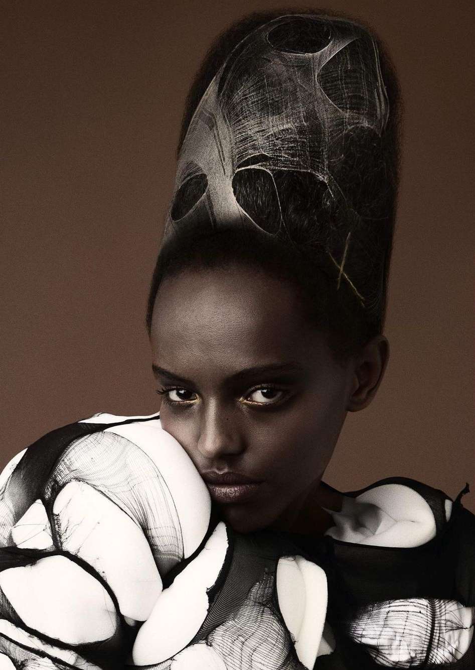Portrait of a Black female model with stylized hair and sculptural black and white clothing in a high fashion studio setting.