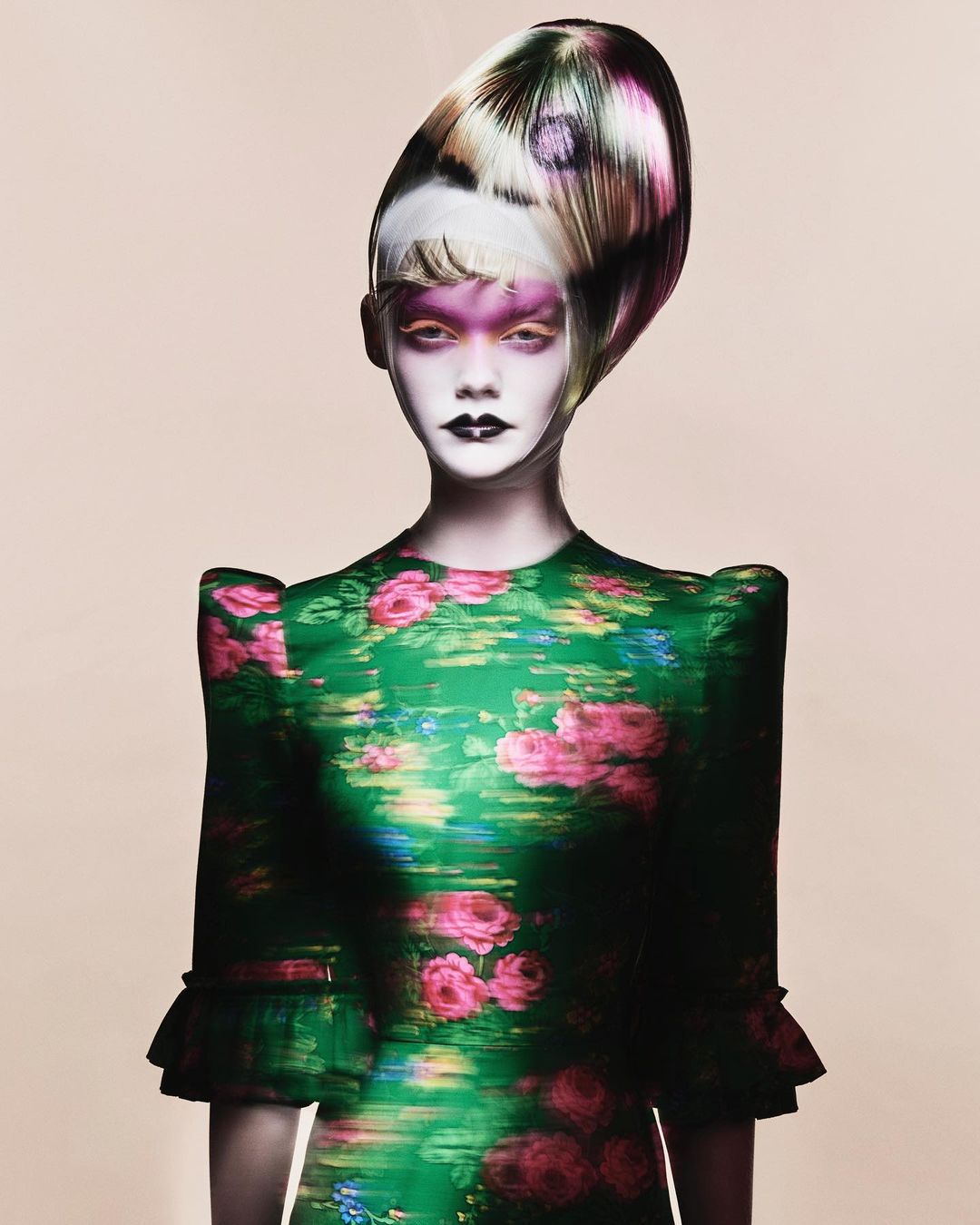 Woman in a green floral dress with dramatic makeup and an extravagant hairstyle, posing against a pale background, haute couture fashion.