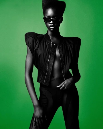 Model in black sunglasses and padded structured jacket against a vibrant green background photographed by Andrew O’Toole.