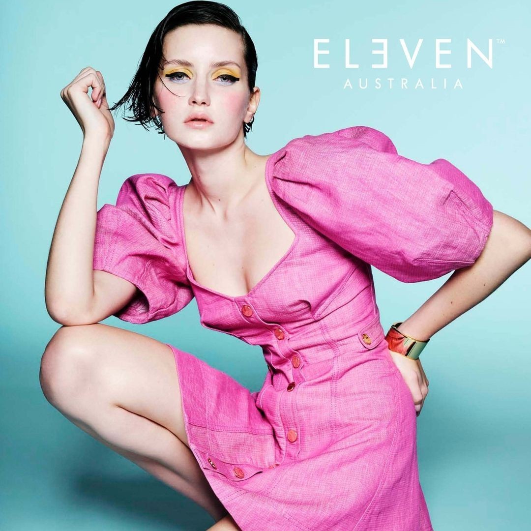 Adult female model with pink dress in a photo studio promotional shoot for Eleven Australia, featuring makeup and modern hair style.