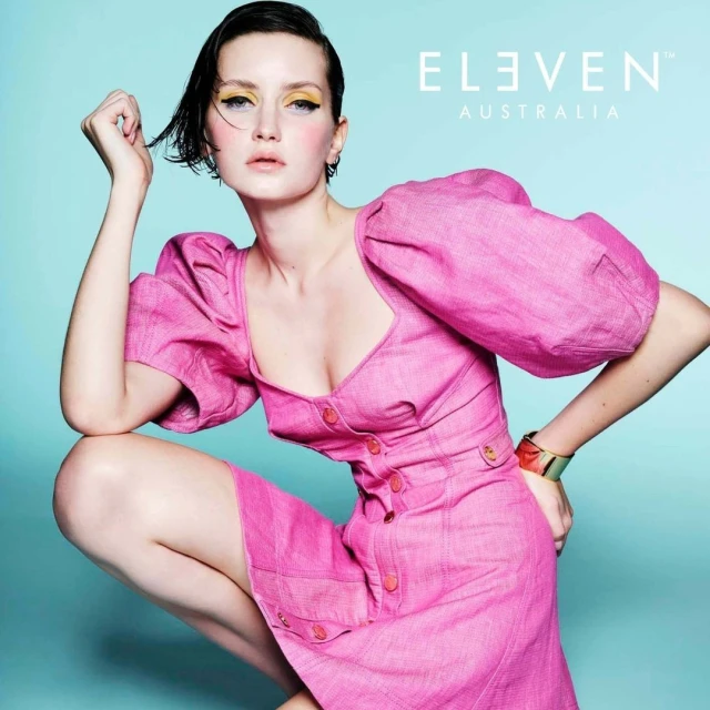 Adult female model with pink dress in a photo studio promotional shoot for Eleven Australia, featuring makeup and modern hair style.
