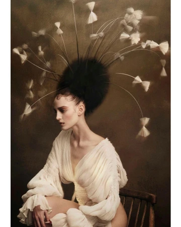 A seated woman wearing an elaborate feather headpiece and a cream dress against a dark textured background by Andrew O'Toole