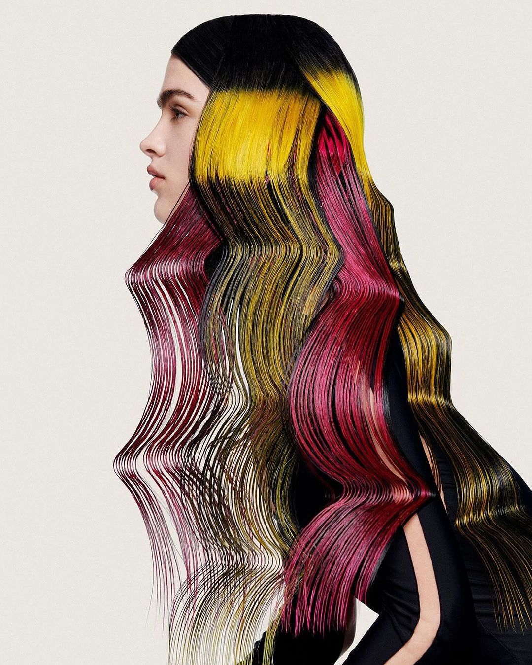 Creative portrait of a woman with long, stylized hair that is dyed in black, yellow, and red hues on an off-white background.