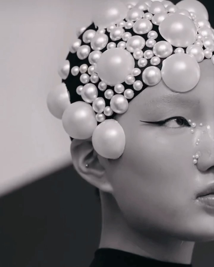 Close-up of a person with artistic makeup and a pearl-covered headpiece, creating a striking beauty and fashion portrait in monochrome.