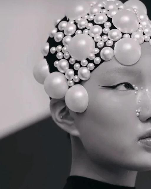 Close-up of a person with artistic makeup and a pearl-covered headpiece, creating a striking beauty and fashion portrait in monochrome.