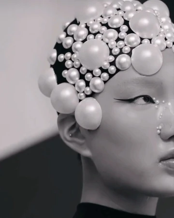 Close-up of a person with artistic makeup and a pearl-covered headpiece, creating a striking beauty and fashion portrait in monochrome.