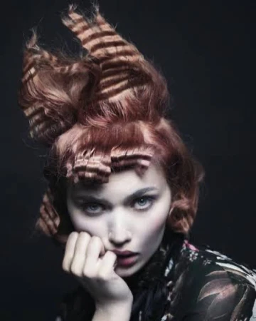 Portrait of a woman with crimped textured hair and dark floral patterned top against a dark background, photographed by Andrew O’Toole.