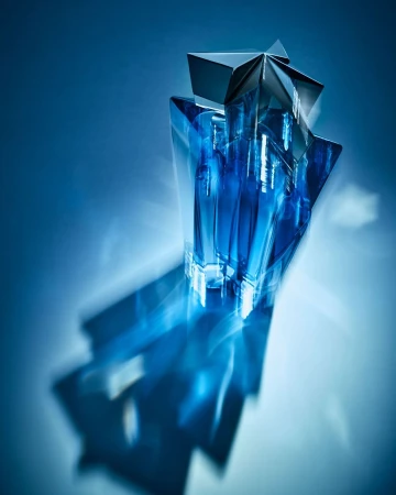 Star-shaped blue glass perfume bottle on a glossy surface with a matching blue background and long shadow, product photography.