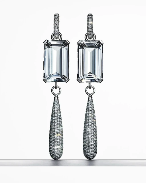 Elegant dangle earrings featuring emerald-cut gemstones and pave diamonds set in silver-tone metal, displayed against a gradient white backdrop.