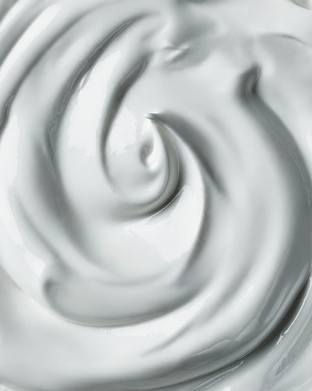 Close-up shot of swirling white cream, lotion, or thick fluid, showcasing its smooth texture and glossy appearance, ideal for beauty or food context.