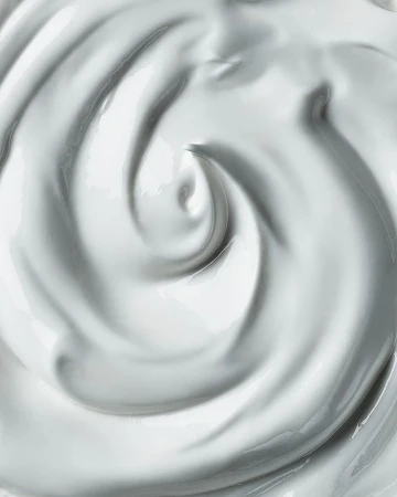 Close-up shot of swirling white cream, lotion, or thick fluid, showcasing its smooth texture and glossy appearance, ideal for beauty or food context.