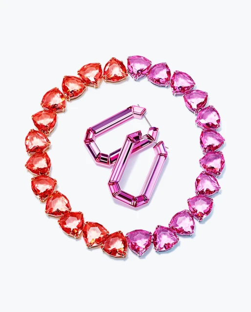 Two pink geometric earrings are displayed within a circle of heart-shaped gems that transition from pink to red on a white background.