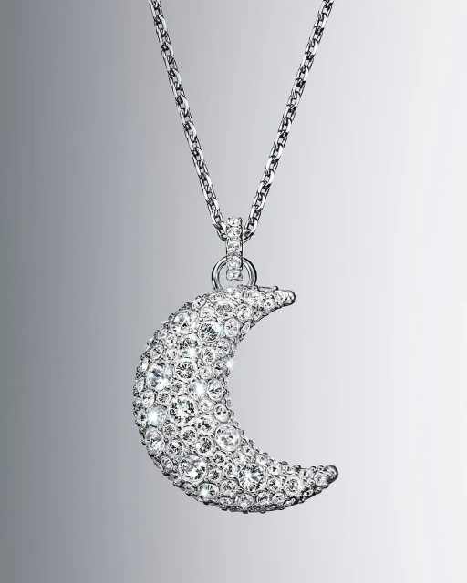 Necklace with a silver chain and a moon-shaped pendant covered in clear crystals, showcased on a neutral grey gradient background.