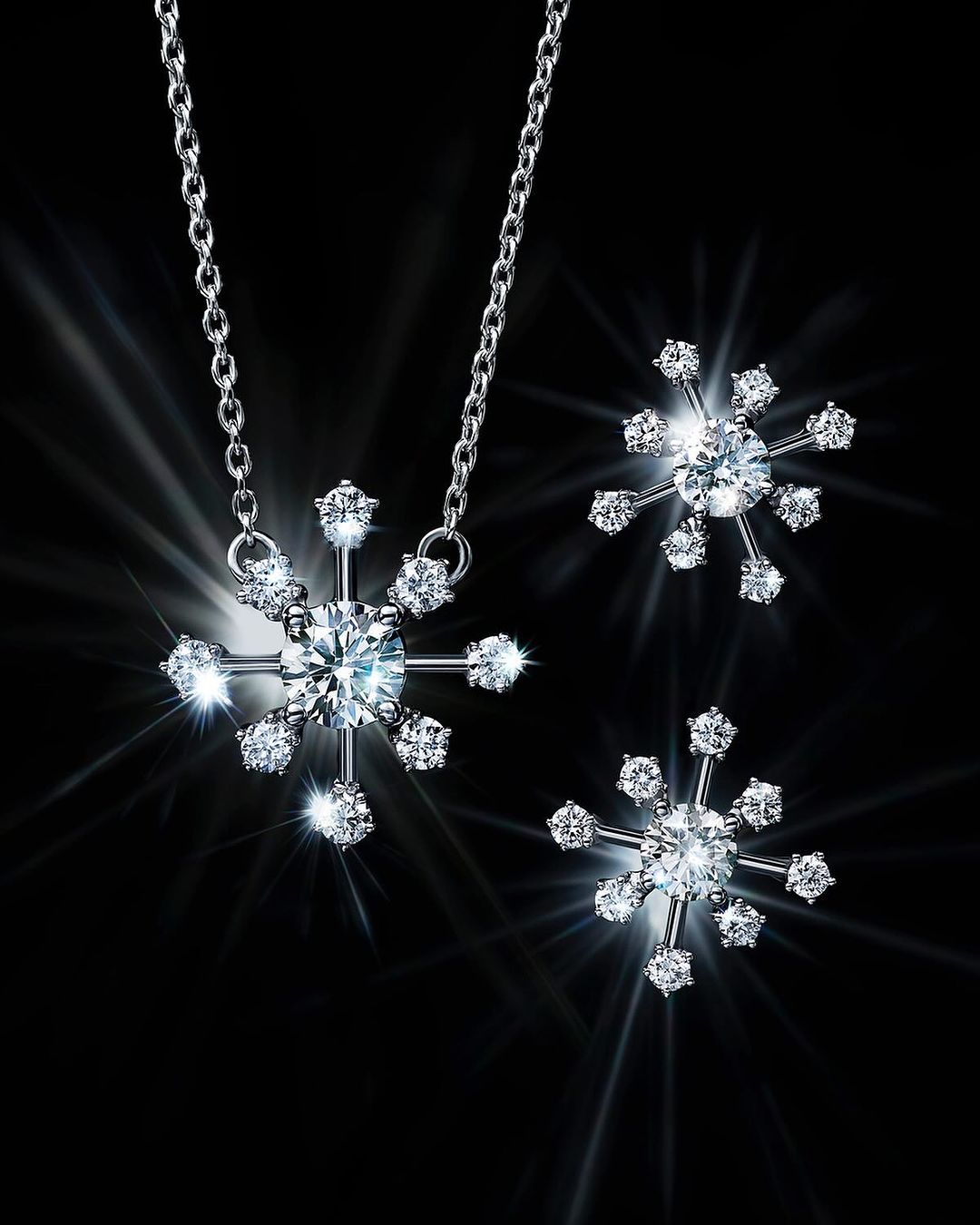 Elegant silver snowflake necklace and earrings sparkle against a dark background with starburst effects, showcasing jewelry design.