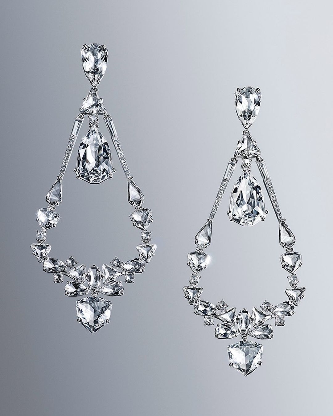 Elegant chandelier earrings sparkle against a gray background. Statement jewelry features clear gemstones in geometric and teardrop shapes.