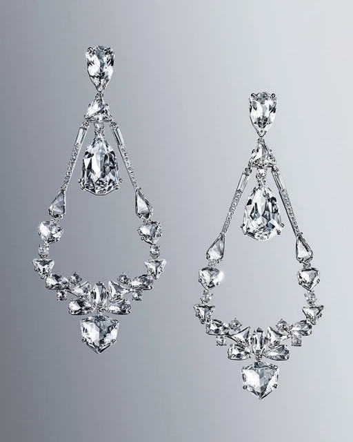 Elegant chandelier earrings sparkle against a gray background. Statement jewelry features clear gemstones in geometric and teardrop shapes.