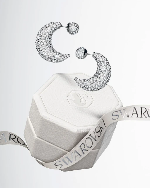 Elevated view of crystal-studded half-hoop earrings displayed over a white gift box, accented by a branded ribbon.