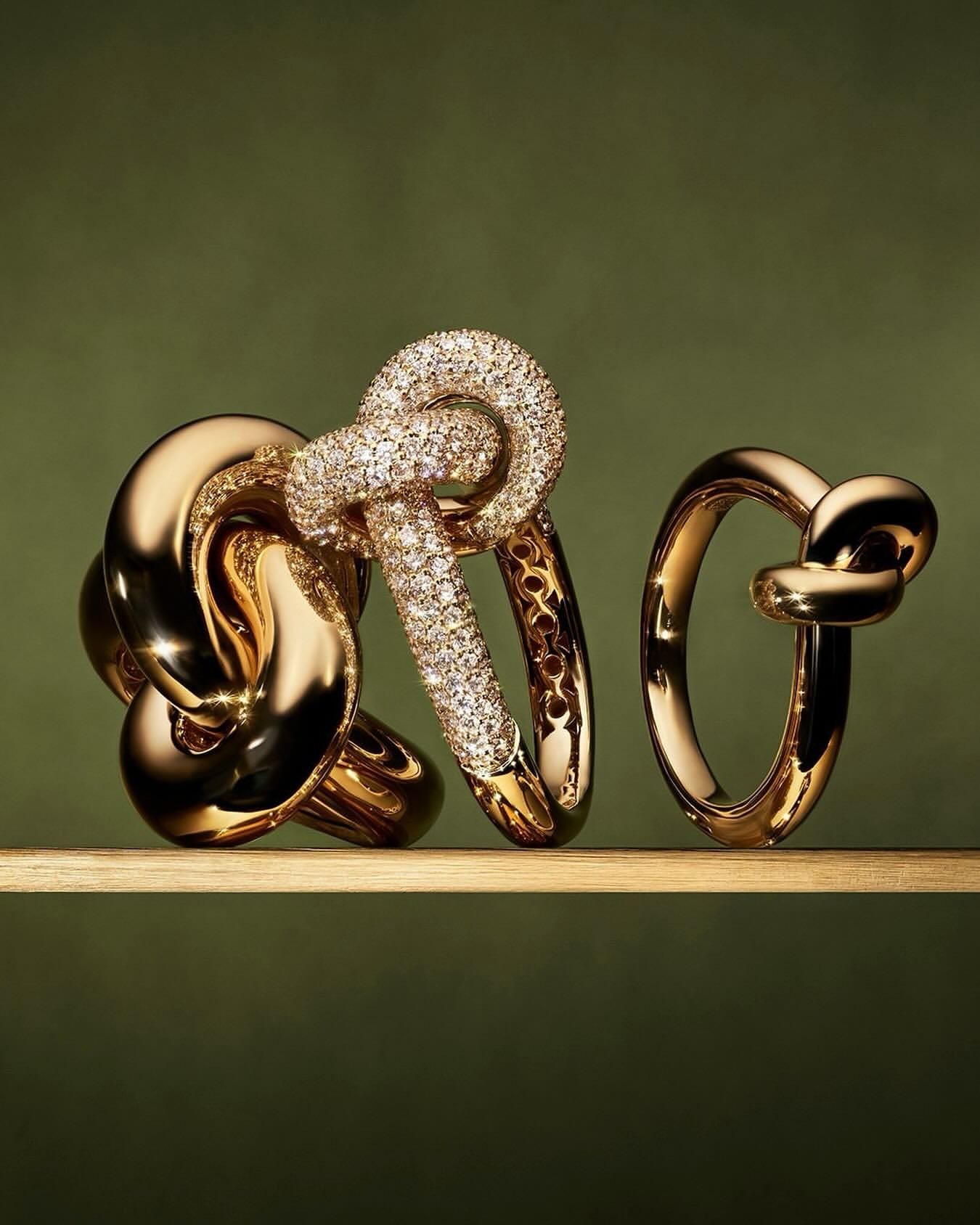 Close-up of three gold and diamond rings of varying sizes on a reflective surface against a green backdrop in a studio setting.