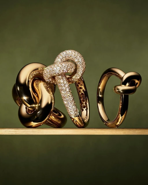 Close-up of three gold and diamond rings of varying sizes on a reflective surface against a green backdrop in a studio setting.